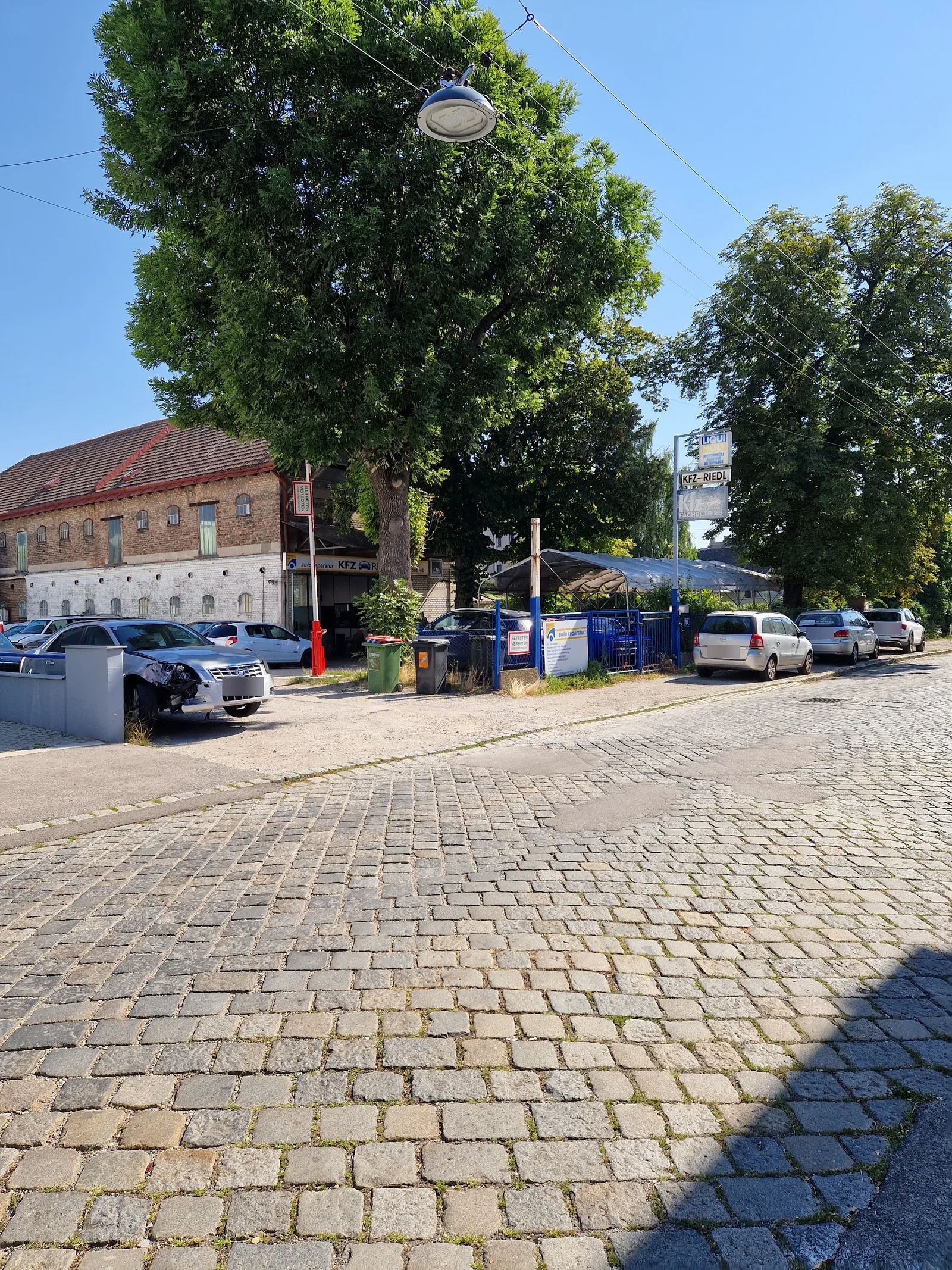 Werkstattgelände mit Schildermast, davor Kopfsteinpflaster